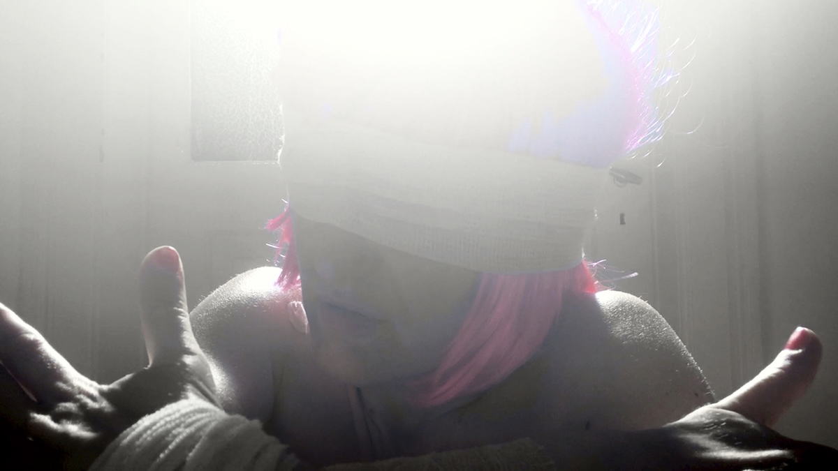 A woman with pink hair and a blindfold is sitting on the floor