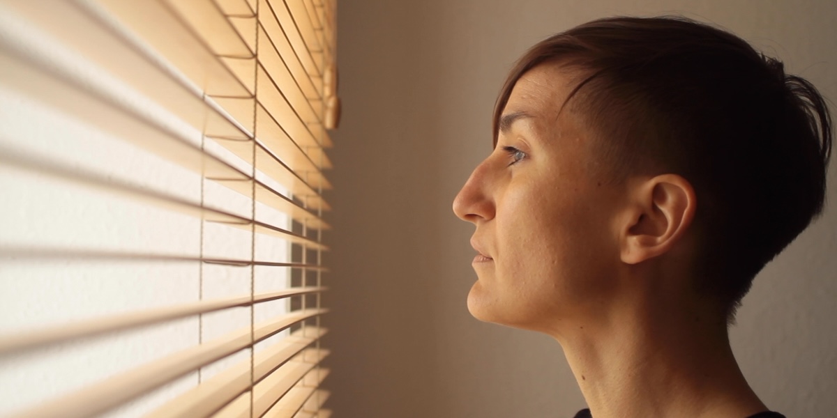 a woman looks out the window trough the blinds